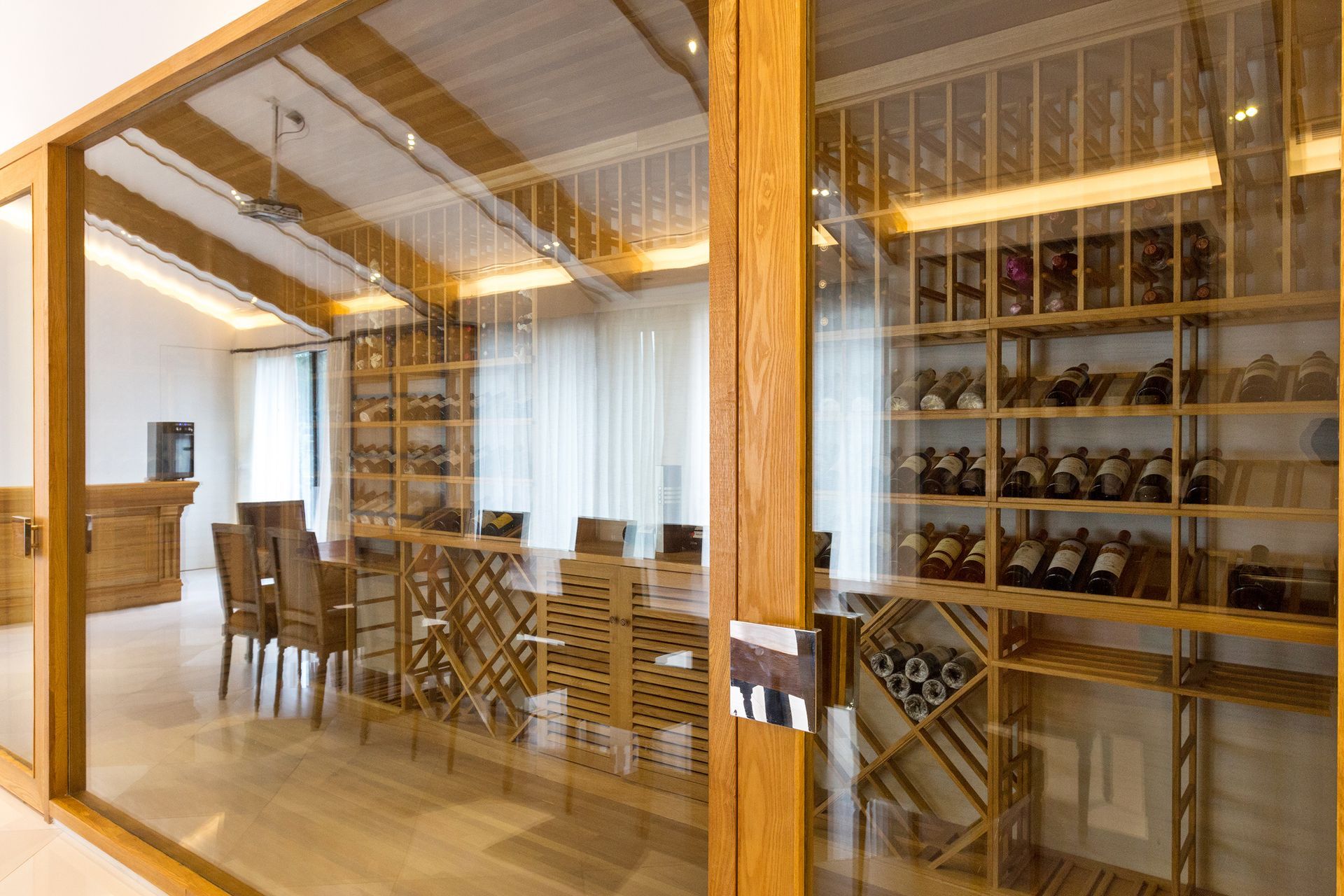 A dining room with a glass wall and a wine cellar filled with bottles of wine.