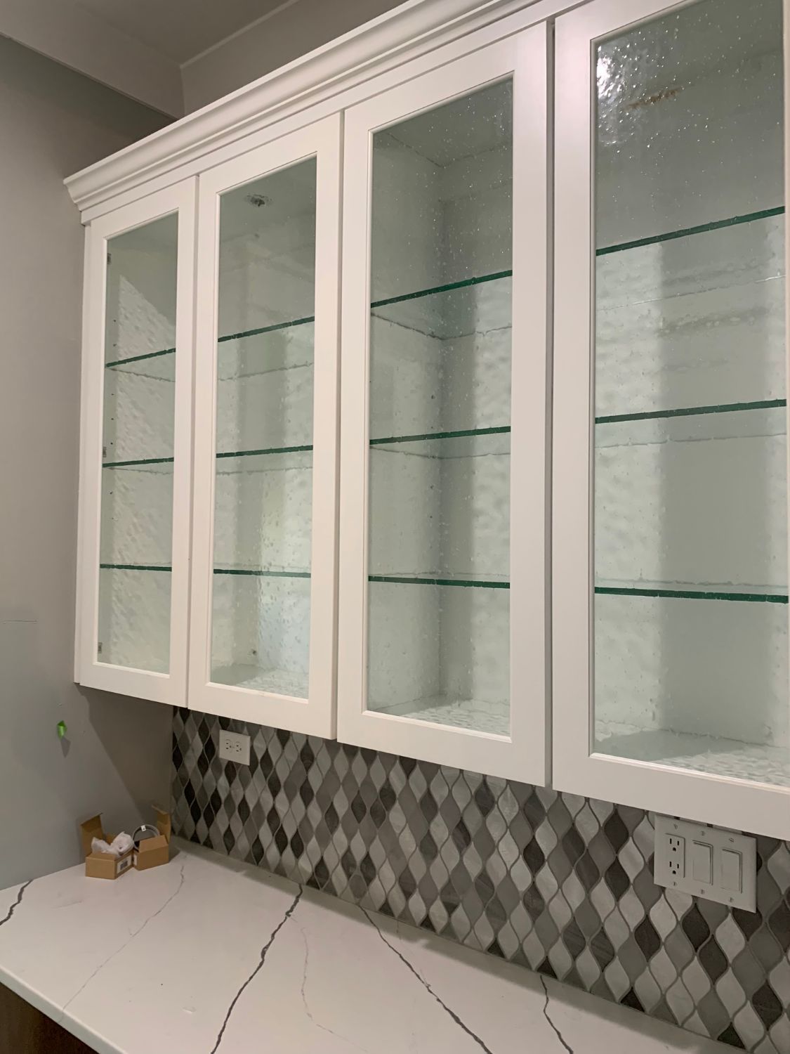 A kitchen with white cabinets and glass doors and shelves.