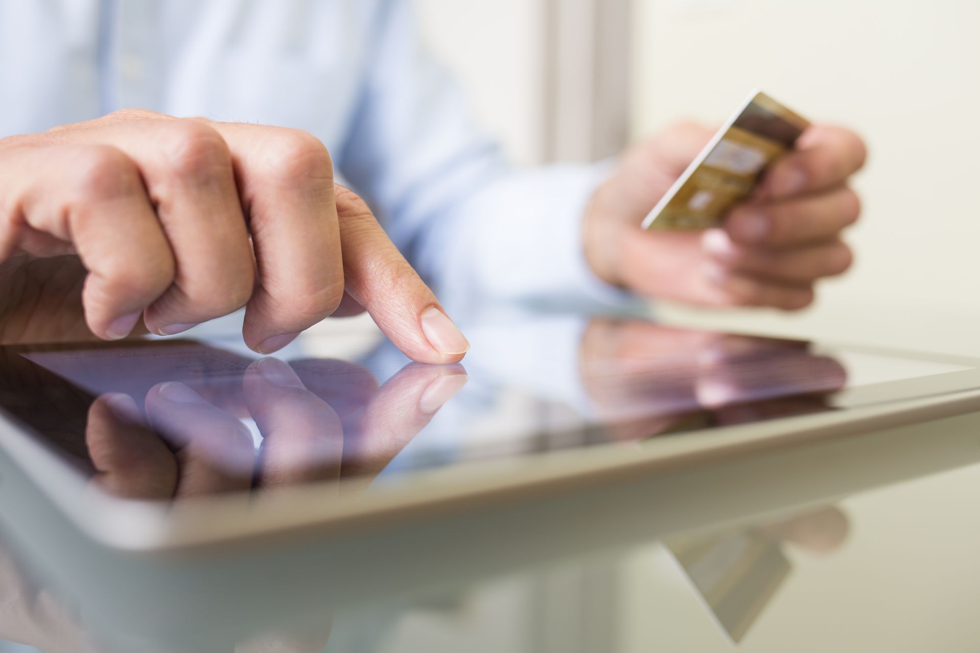 Person's hands using a tablet while holding a gold credit card.