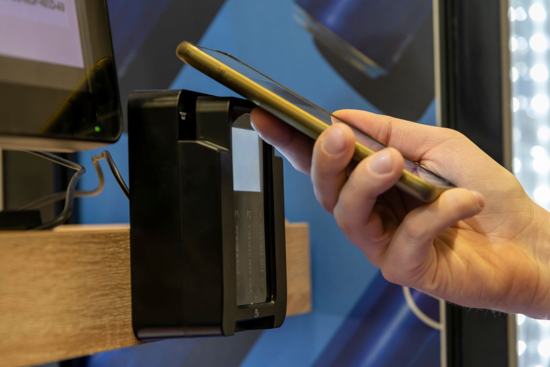 Hand holding a phone over a black payment reader for contactless payment at a store.