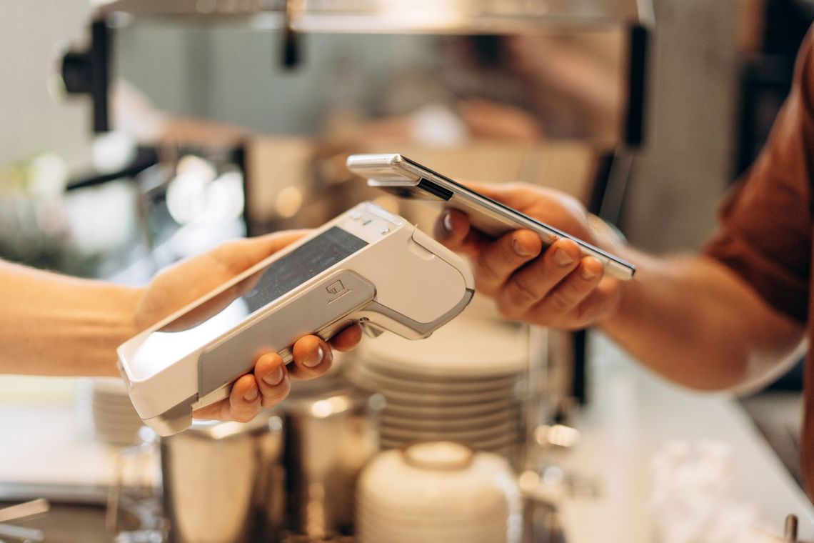 Person paying with phone at a point-of-sale terminal in a cafe.