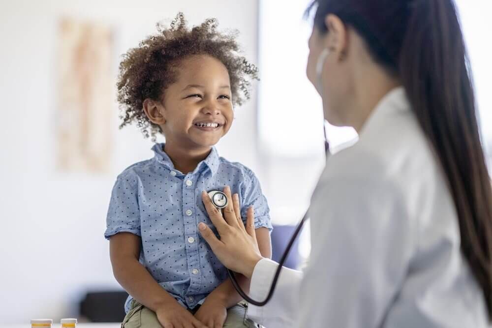 Boy smiles while doctor listens to his heart with a stethoscope in medical office.