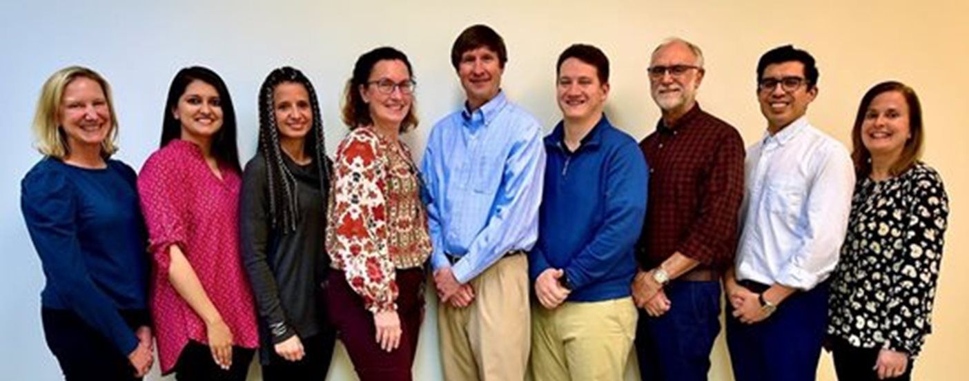 Group of people smiling, standing against a white and yellow gradient background.