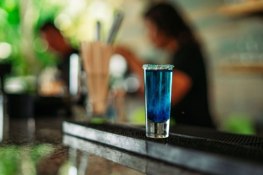 A shot of blue liquid is sitting on a bar counter.