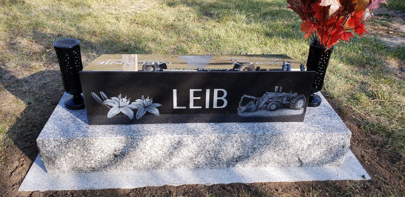 Black headstone with the name LEIB, floral carvings, and a vehicle. On a granite base.