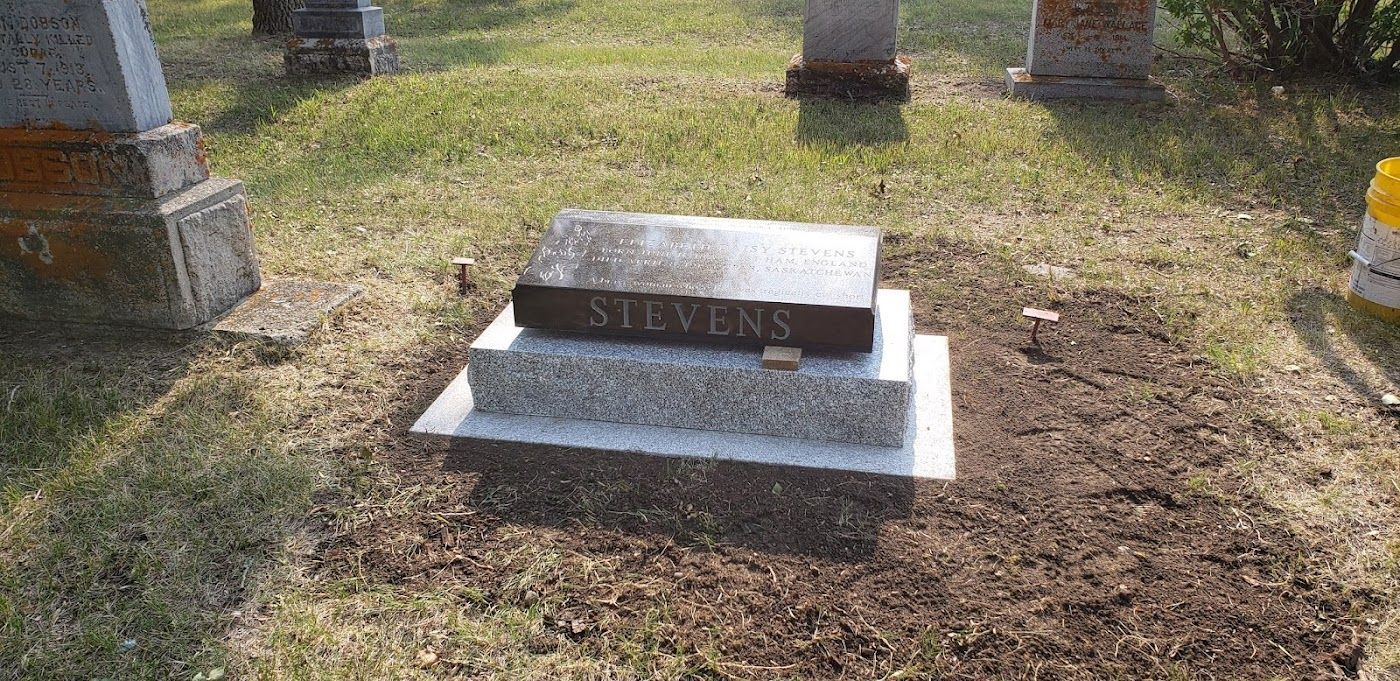 Grave in a cemetery with a dark rectangular headstone that reads 