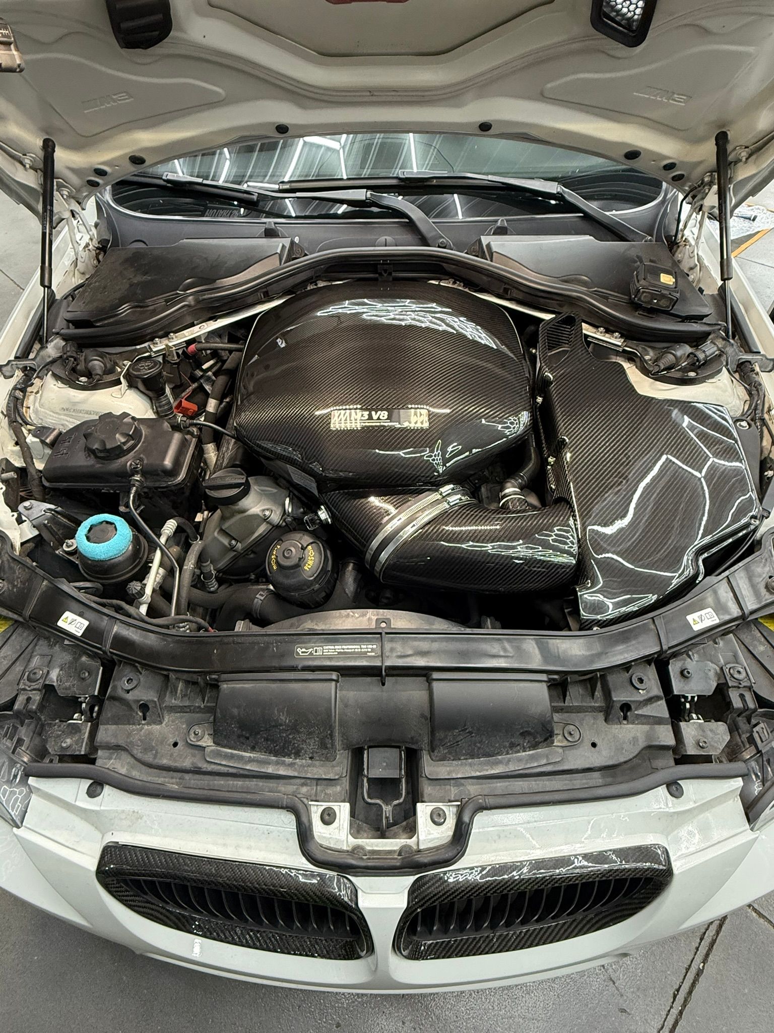 Open car hood reveals a black and carbon fiber engine bay.