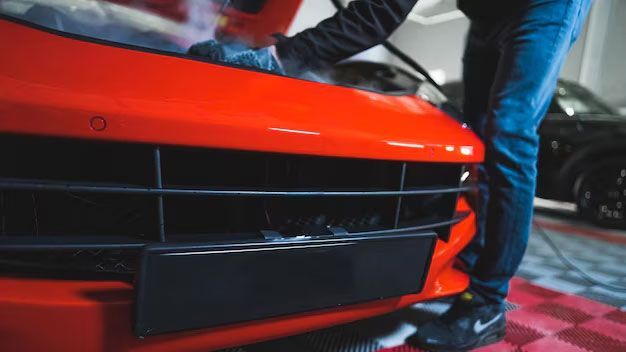 Close-up of a bright red vintage sports car front end, showing the wheel, bumper, headlights, and part of a license plate.