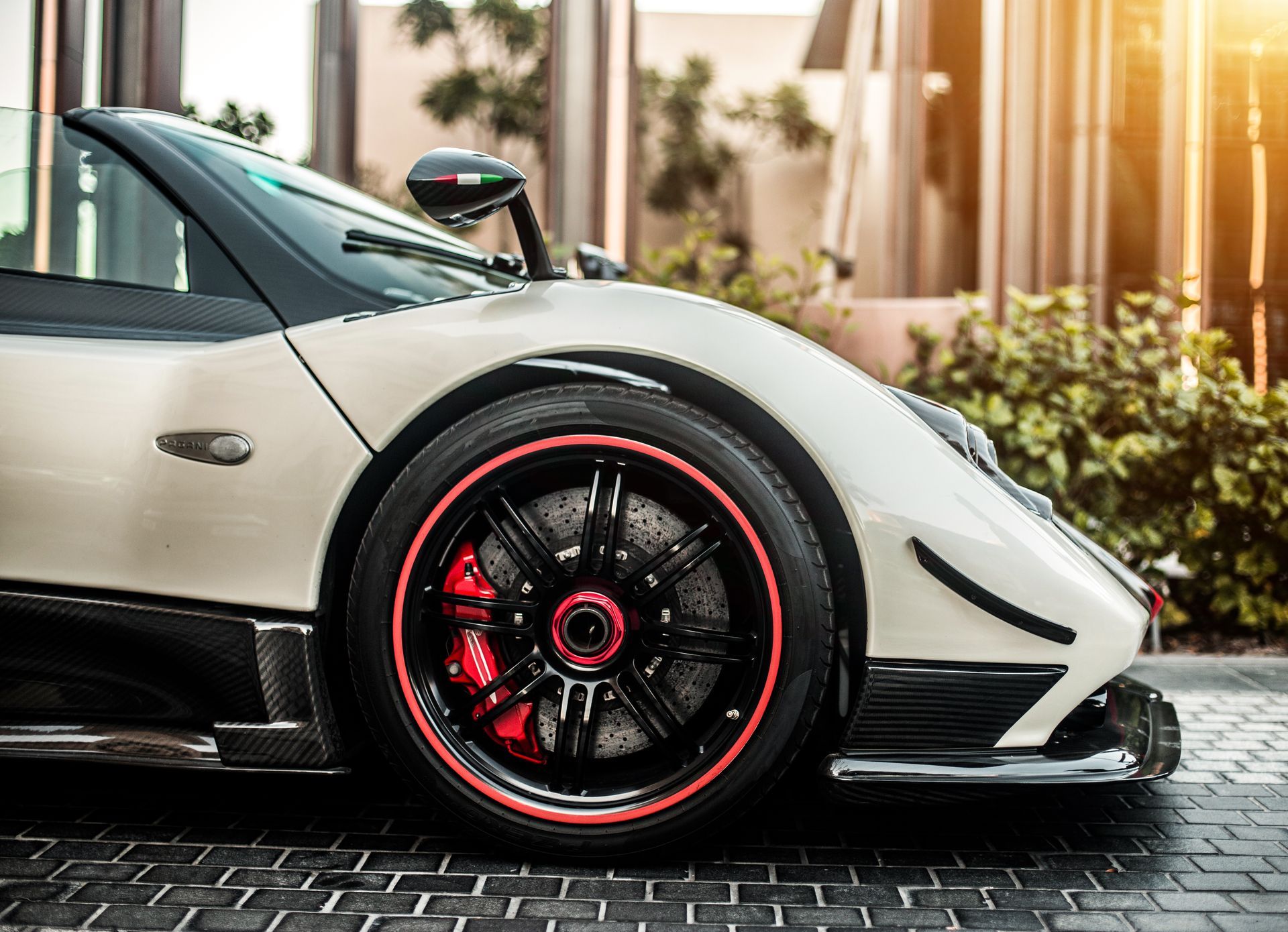 Close-up side view of a cream-colored luxury Pagani supercar with a black wheel, red brake calipers, and a carbon fiber trim.