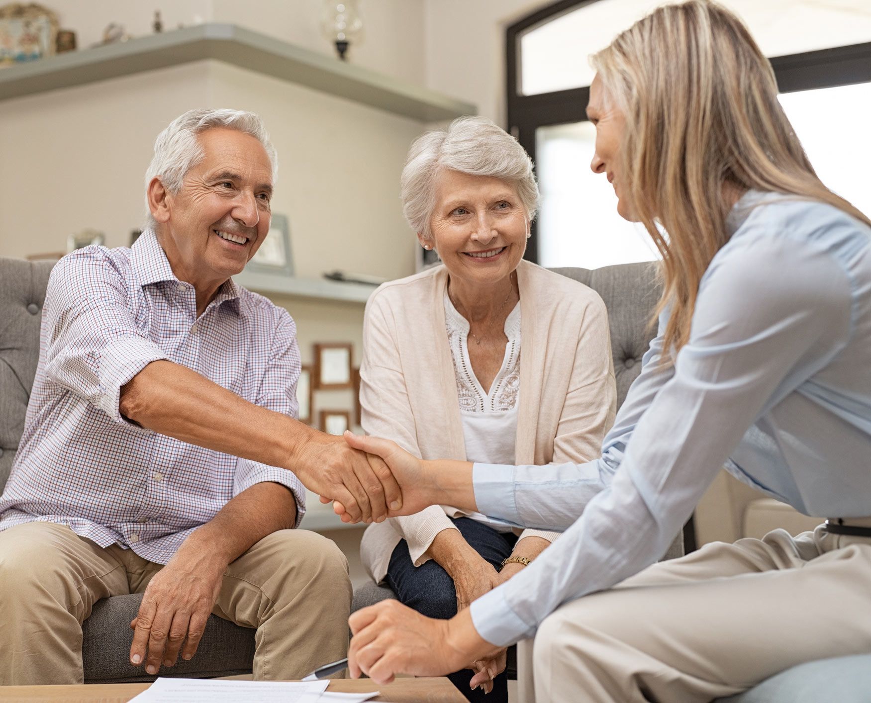 Senior couple shaking hands with a woman on a sofa, smiling.