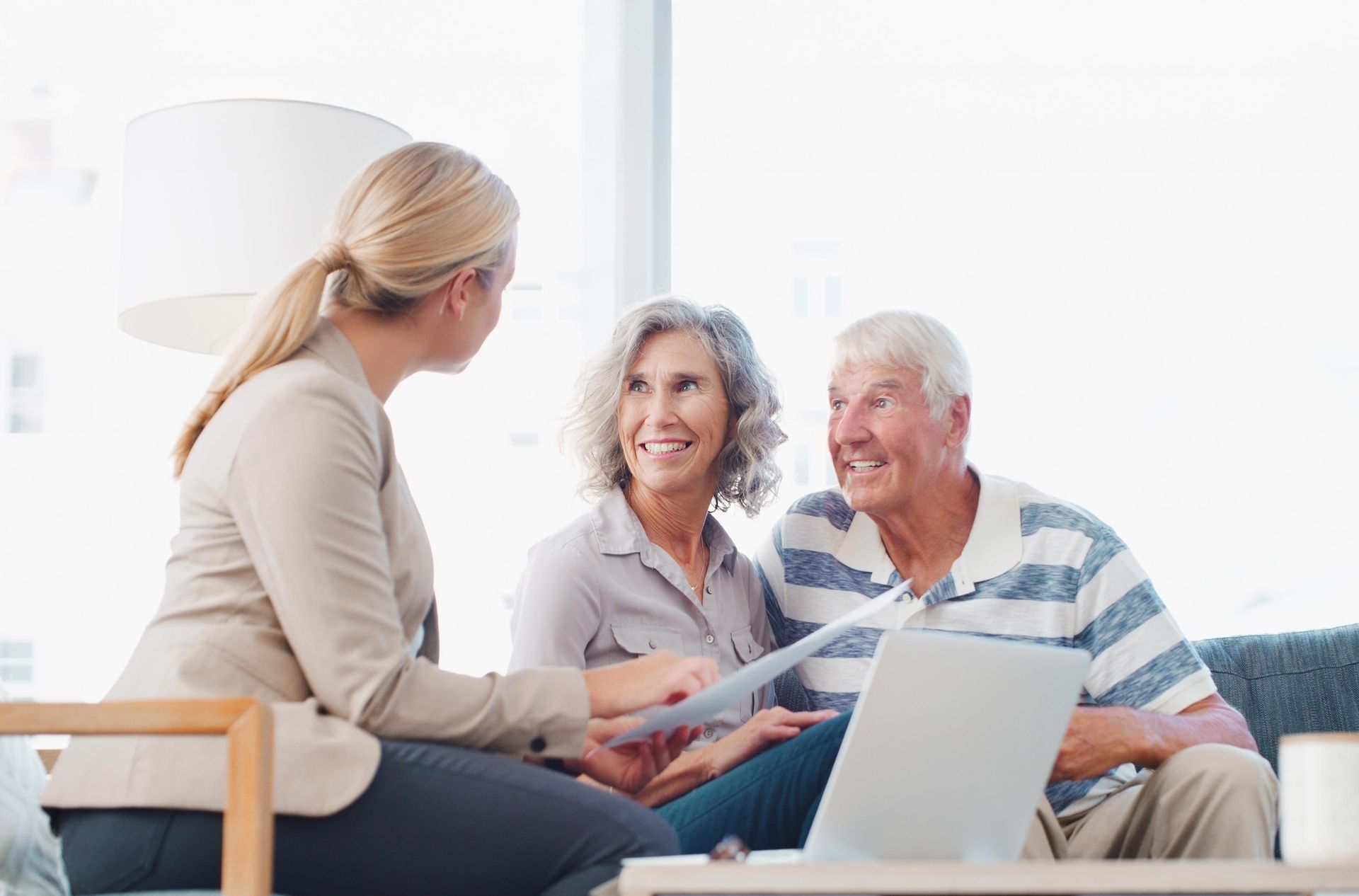 Financial advisor showing documents to a smiling, older couple in a well-lit living room.