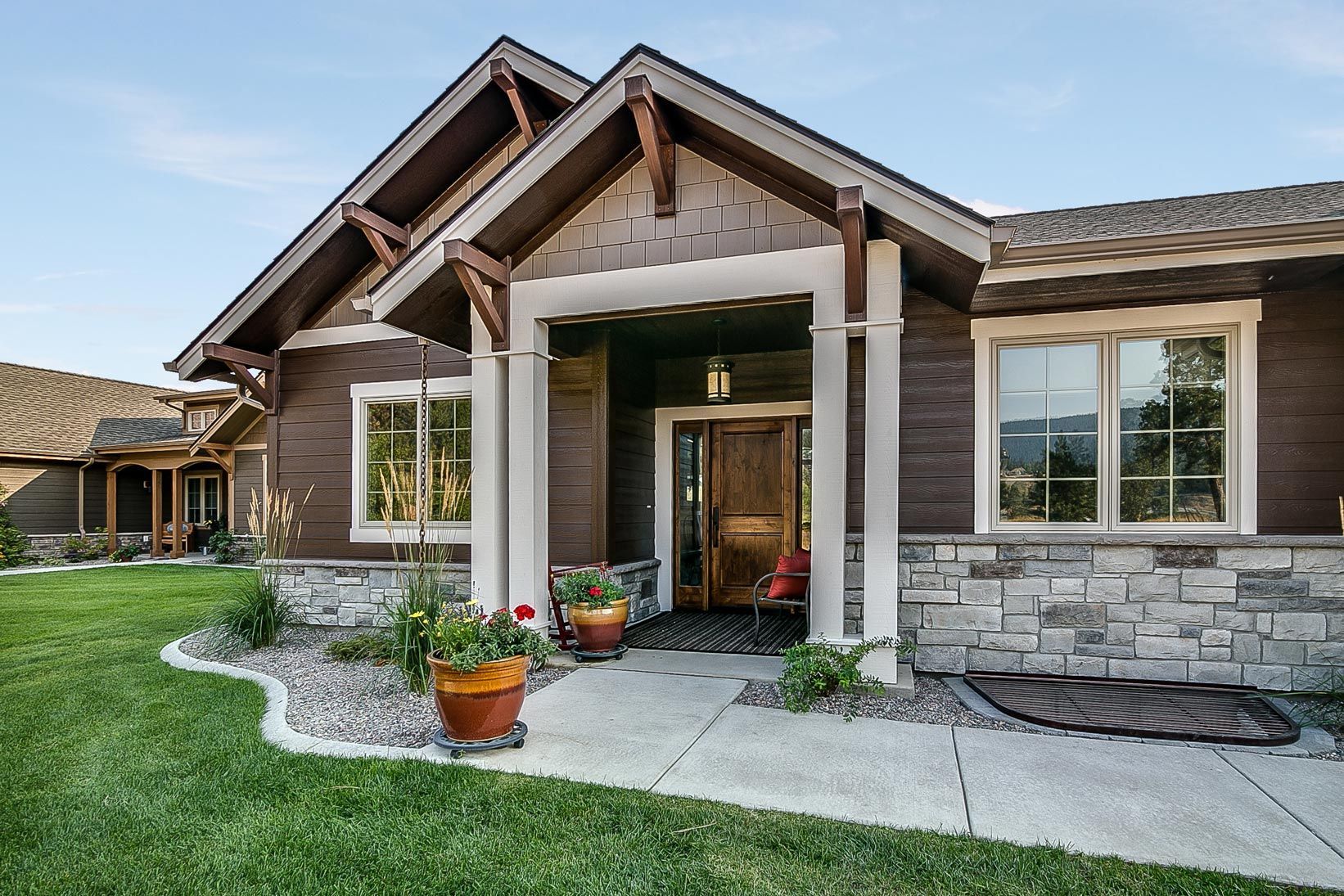 Brown house with stone accents, arched entryway, and green lawn.
