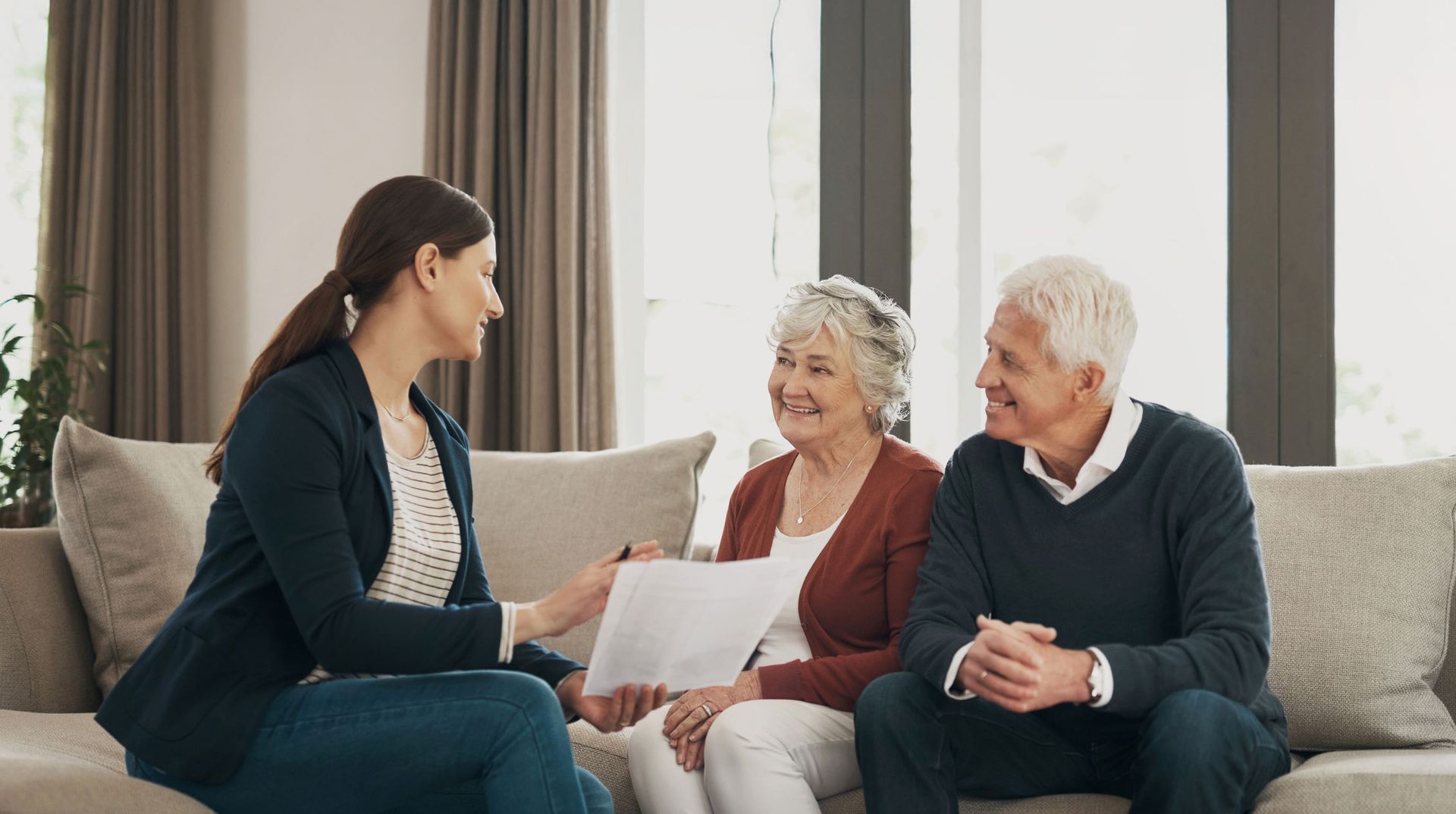 Woman showing paperwork to an older couple on a sofa. They all smile, in a living room.