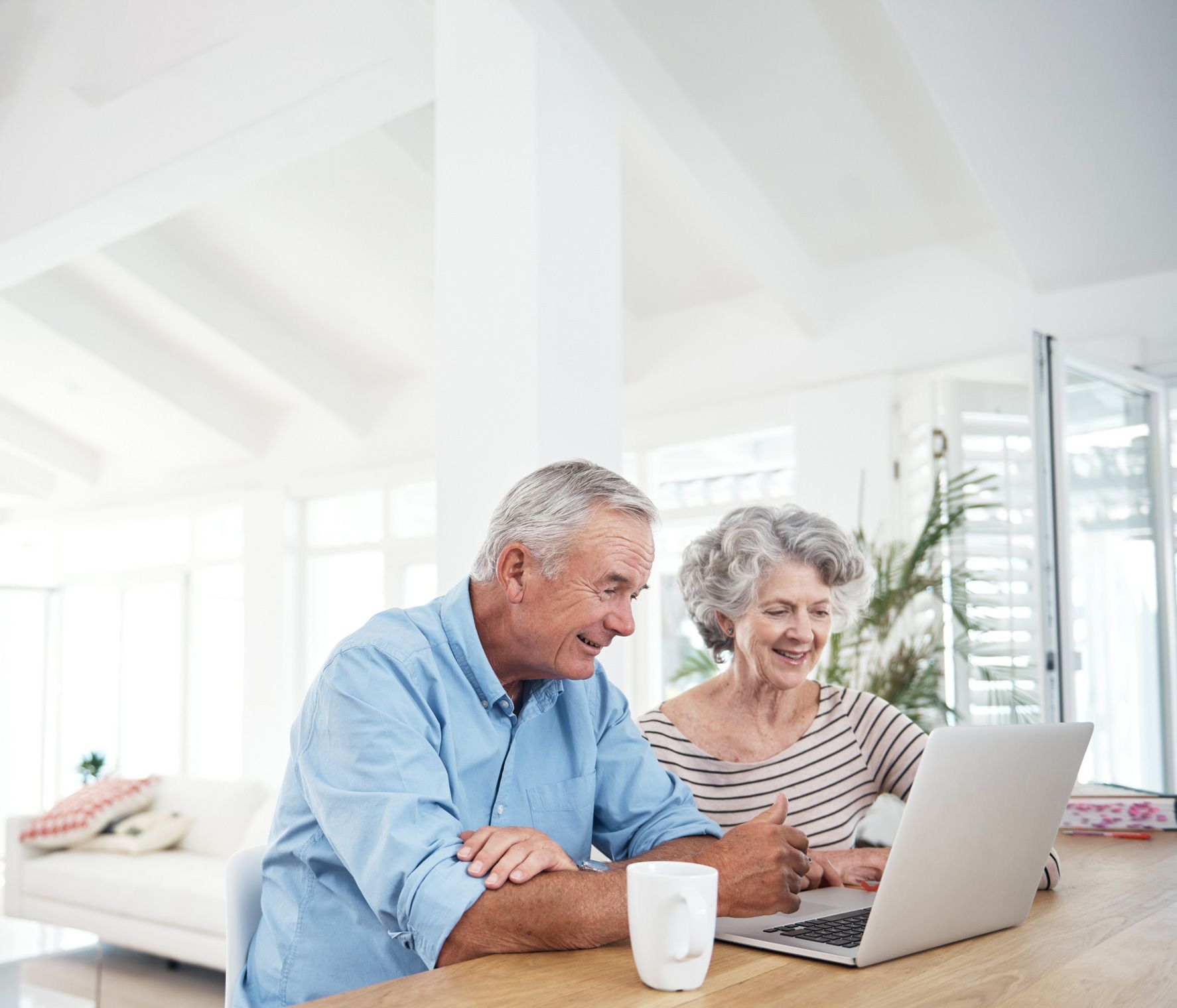 Older couple smiling while looking at a laptop computer. Indoors, bright room.