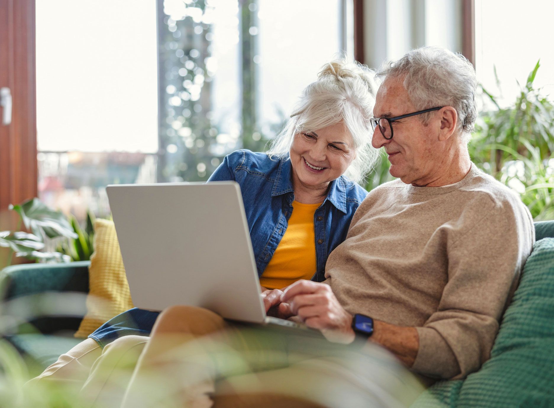 Smiling couple looking at laptop on a couch in a bright living room.