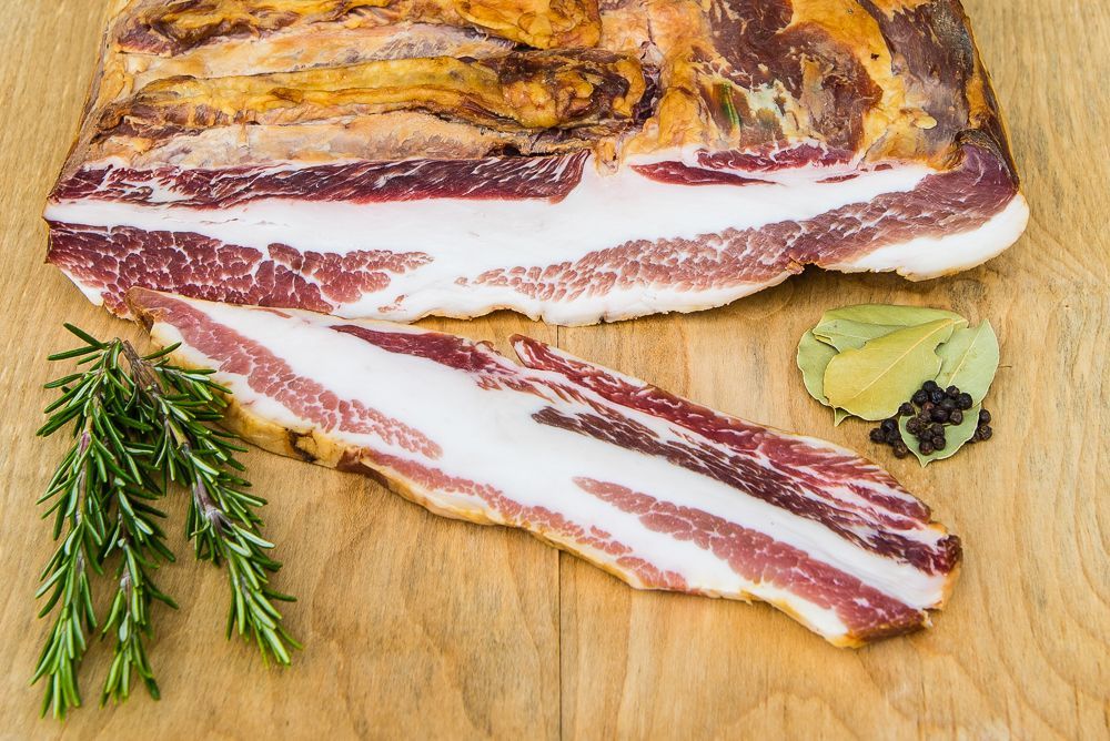 Ein Stück Speck liegt auf einem hölzernen Schneidebrett.