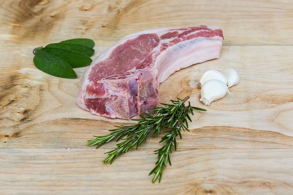 Ein Stück Duroc auf einem Holzschneidebrett mit Knoblauch und Rosmarin.