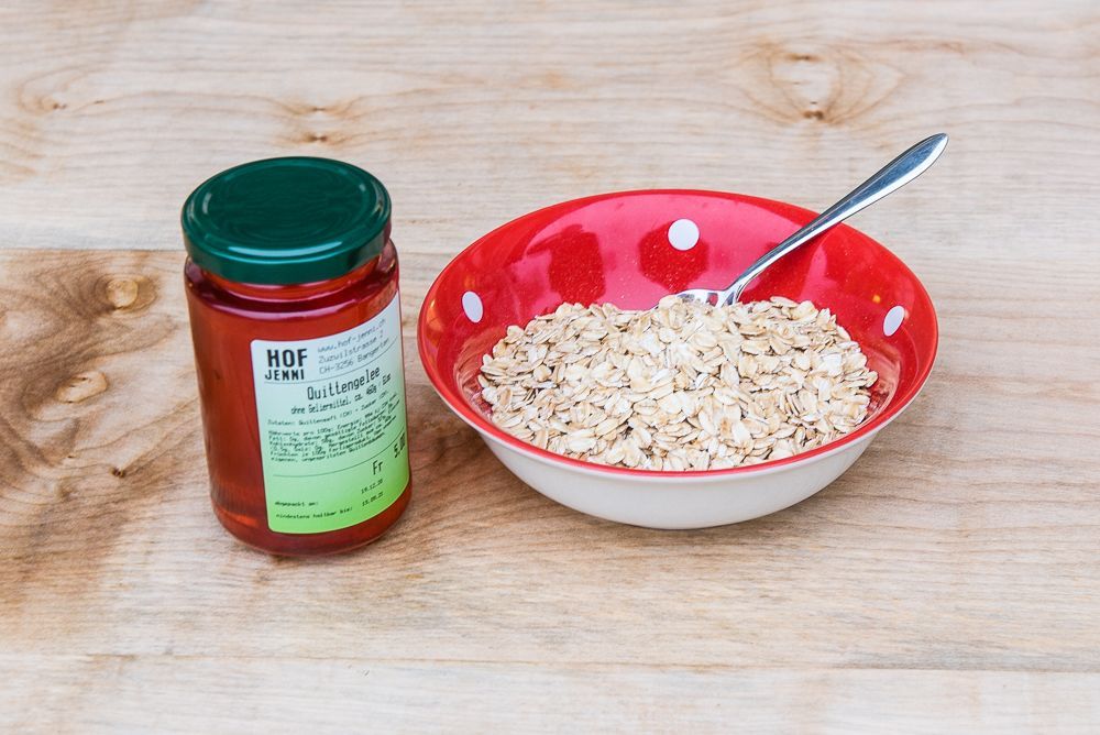 Eine Schüssel Haferbrei neben einem Glas Honig auf einem Holztisch.