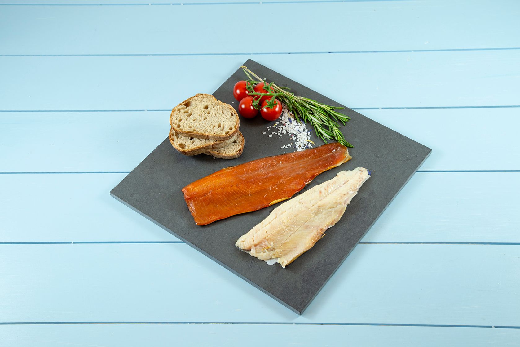 Ein Teller mit Fisch, Brot und Tomaten auf einem Tisch.