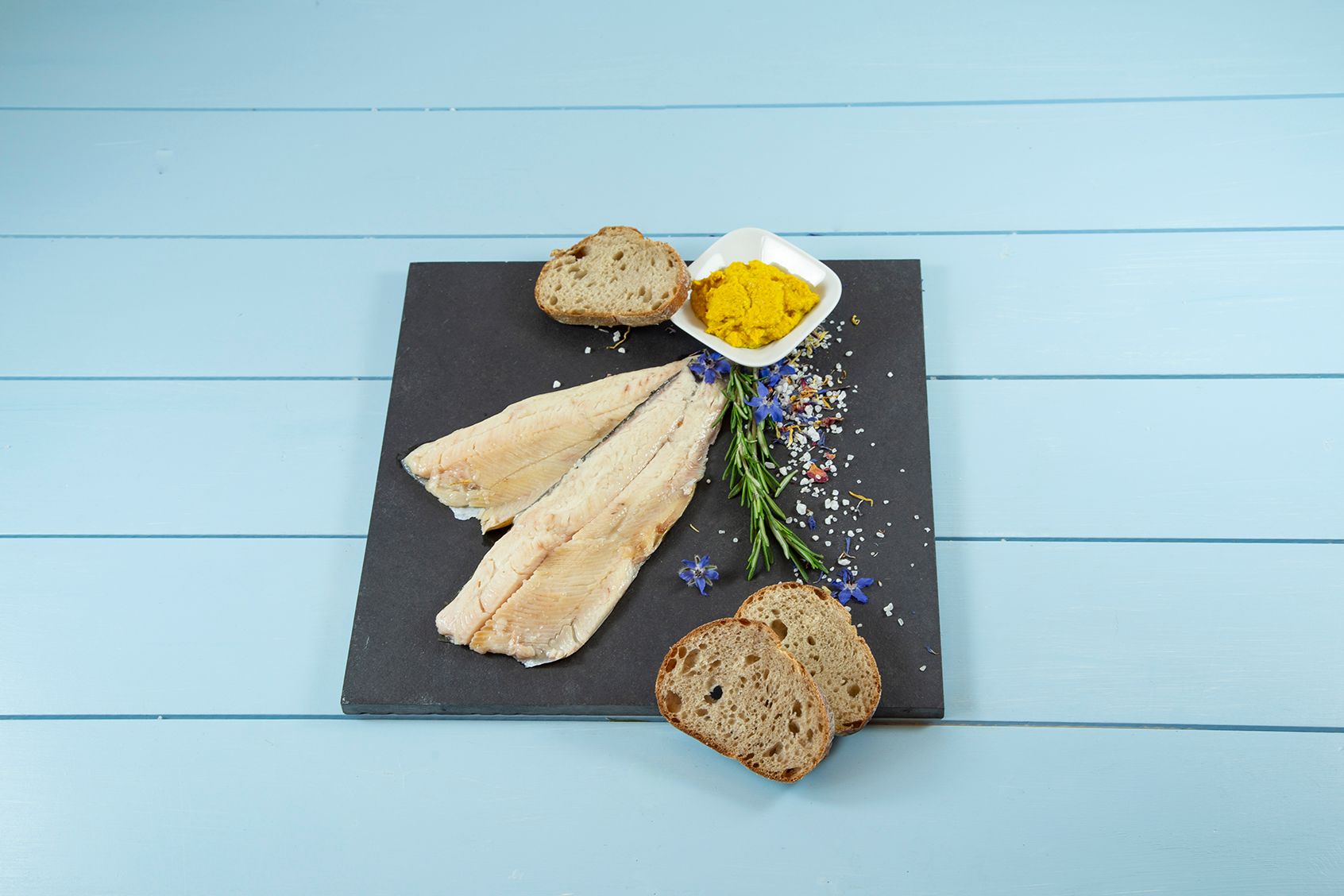 Ein Teller mit Fisch, Brot und Senf auf einem Tisch.