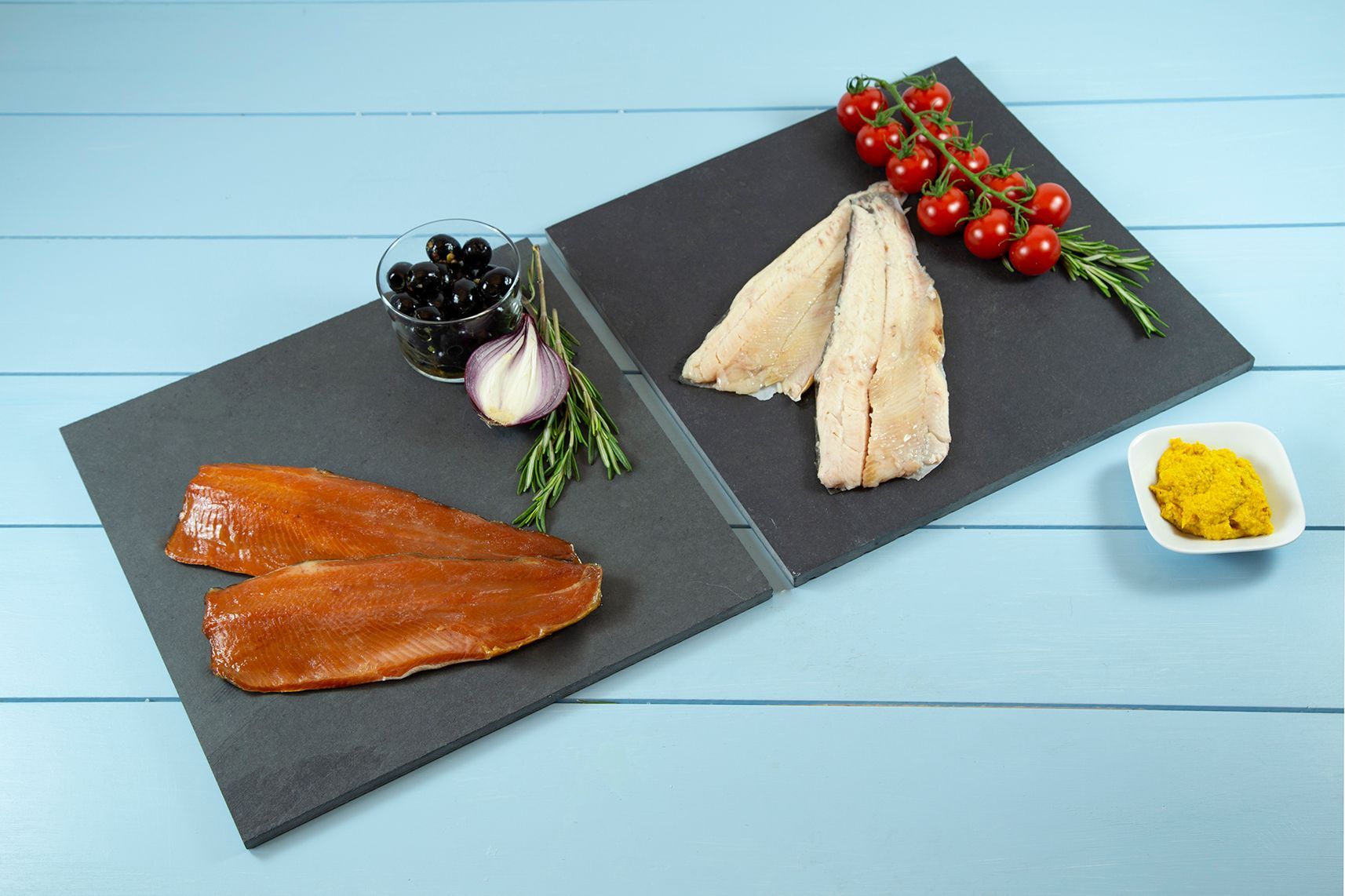 Zwei Teller mit Tomaten, Oliven, Knoblauch, Senf und Fisch auf einem Tisch.