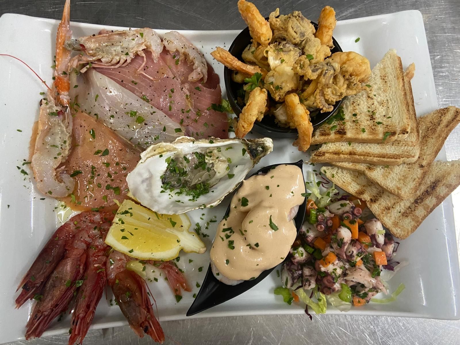 Un piatto bianco sormontato da una varietà di frutti di mare e pane