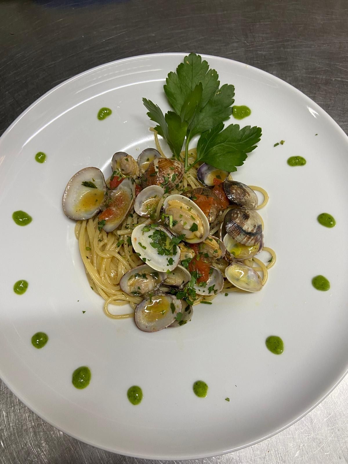 Un piatto bianco con sopra spaghetti e vongole su un tavolo.