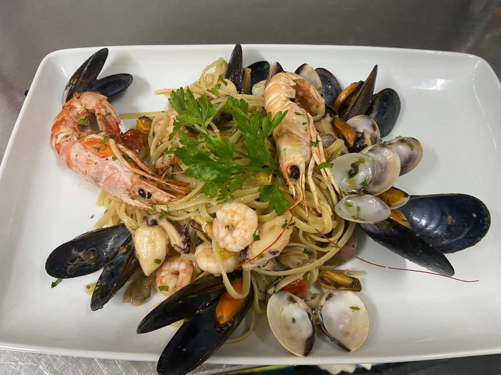 Un piatto bianco con sopra tagliatelle, gamberi, cozze e prezzemolo.
