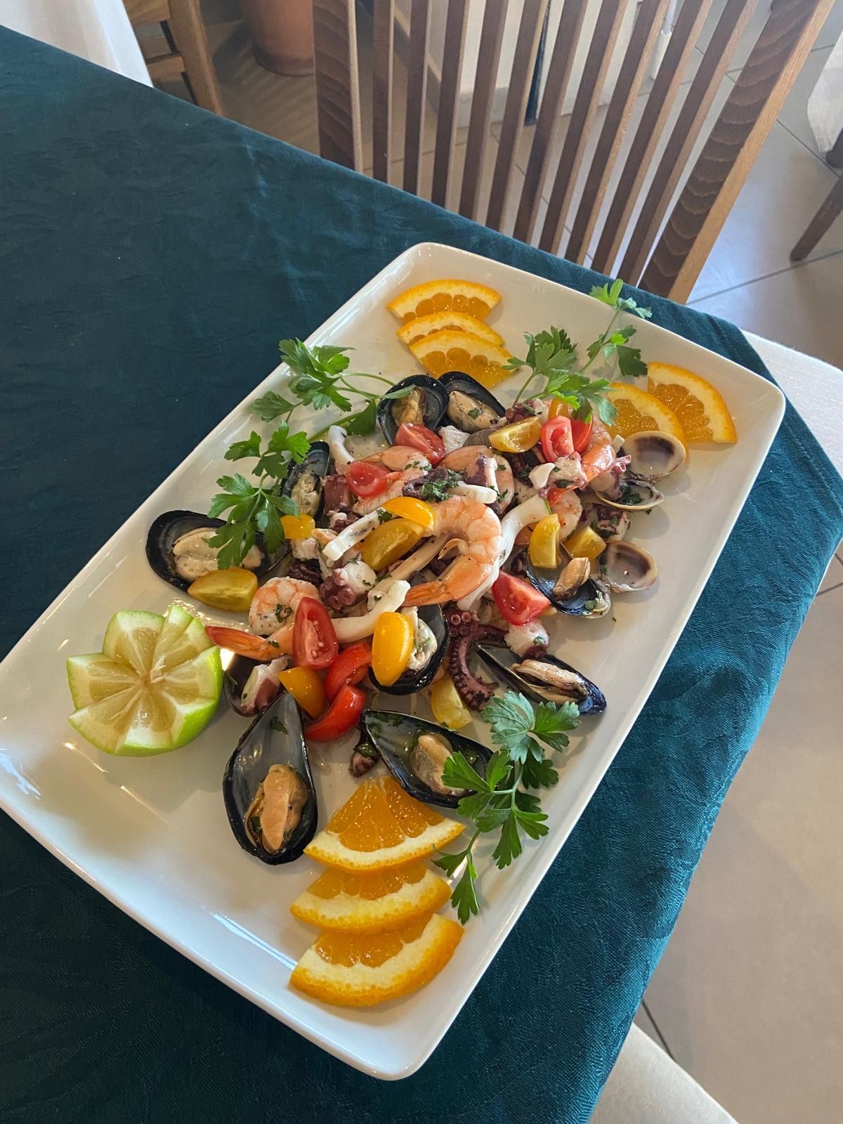 Un piatto bianco con frutti di mare e fette d'arancia su un tavolo.