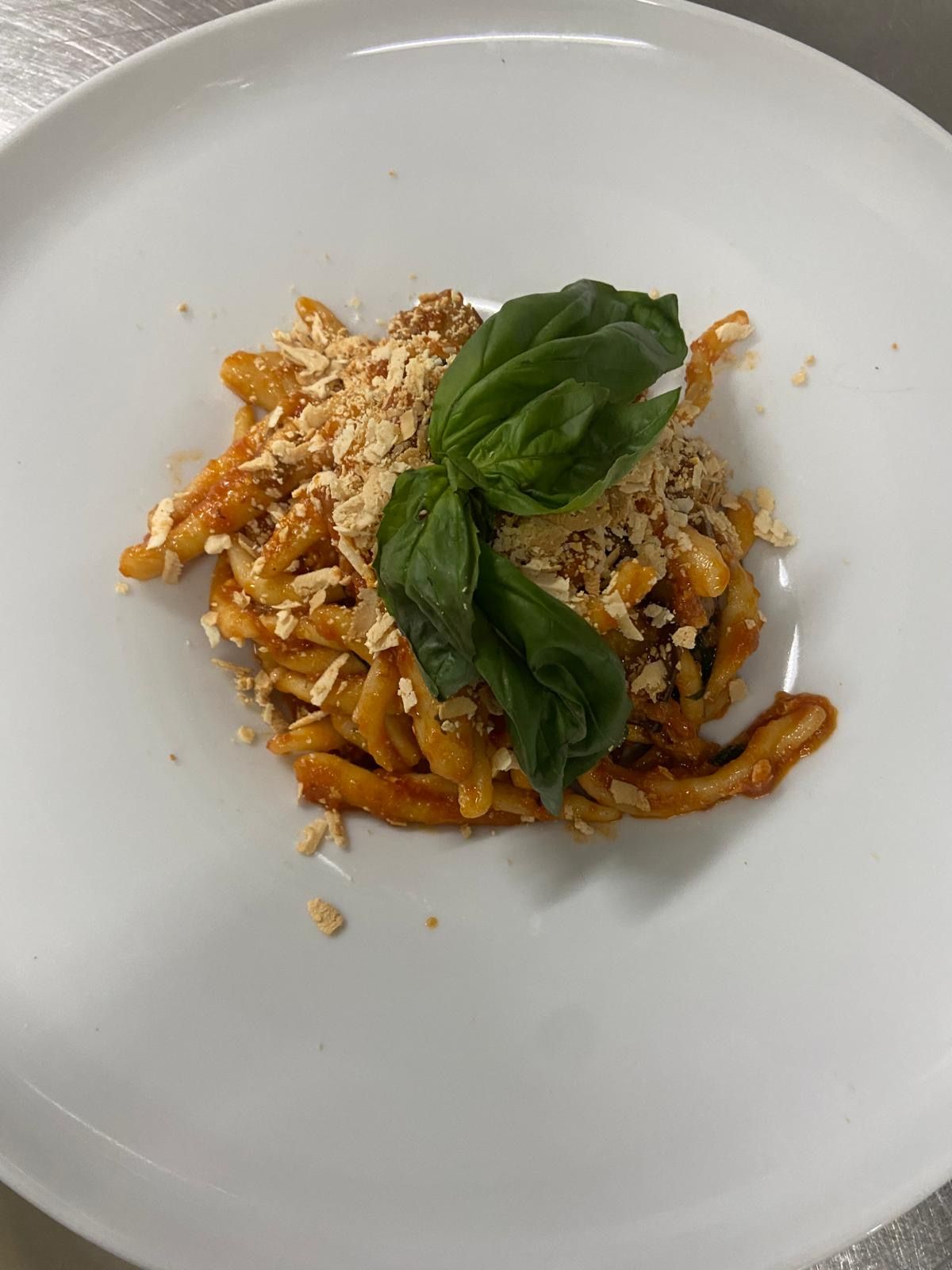 Un piatto bianco con pasta e basilico su un tavolo.