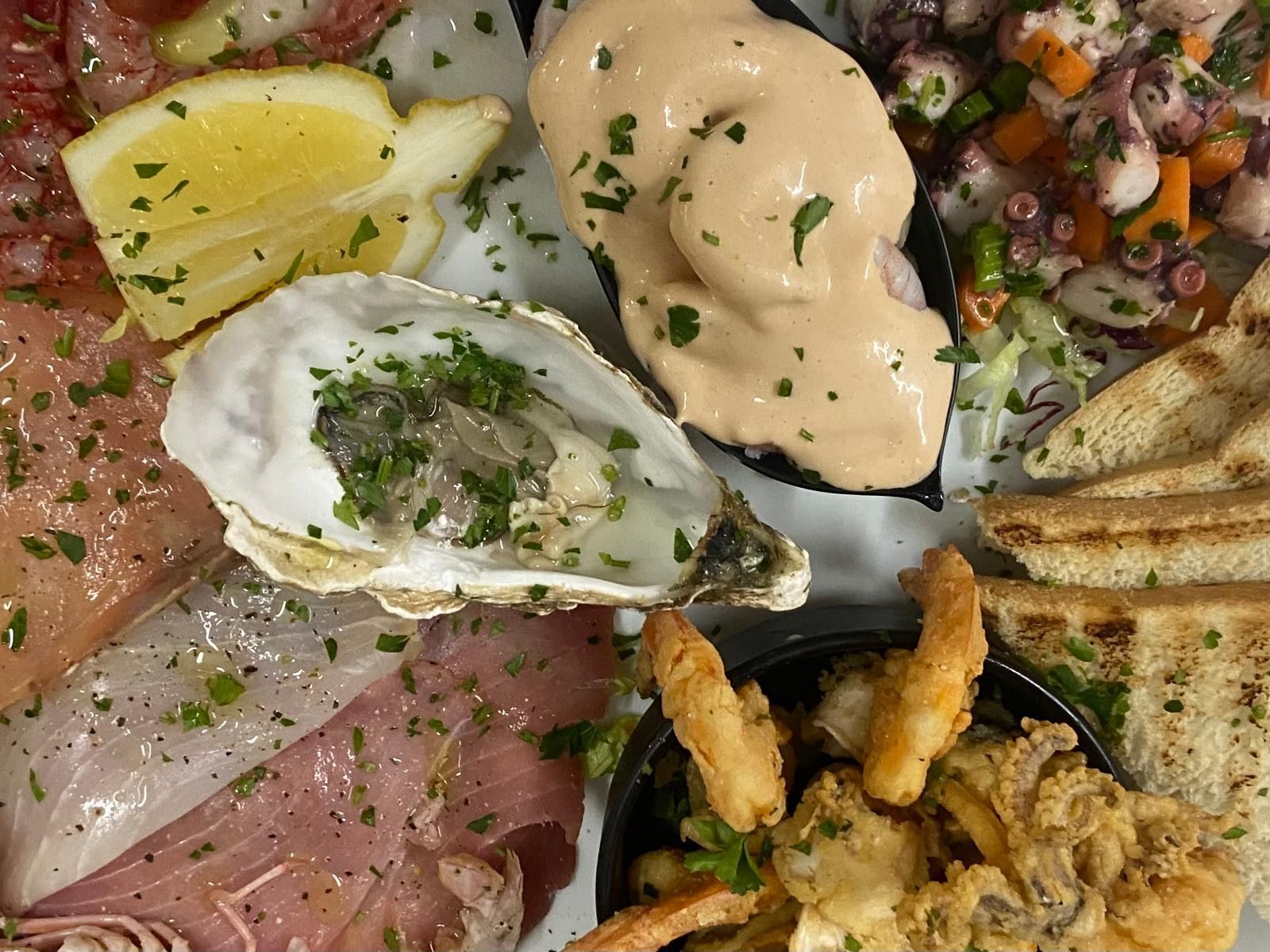 Un piatto di cibo con ostriche, gamberi, pane e salsa su un tavolo.