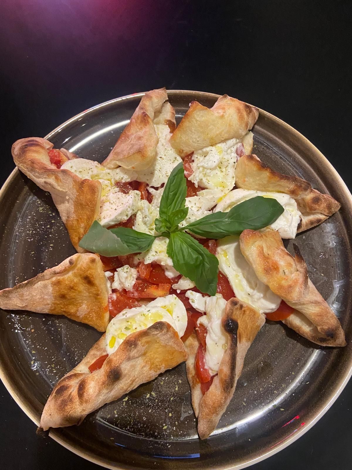 Una pizza con pomodori, mozzarella e basilico su un piatto.