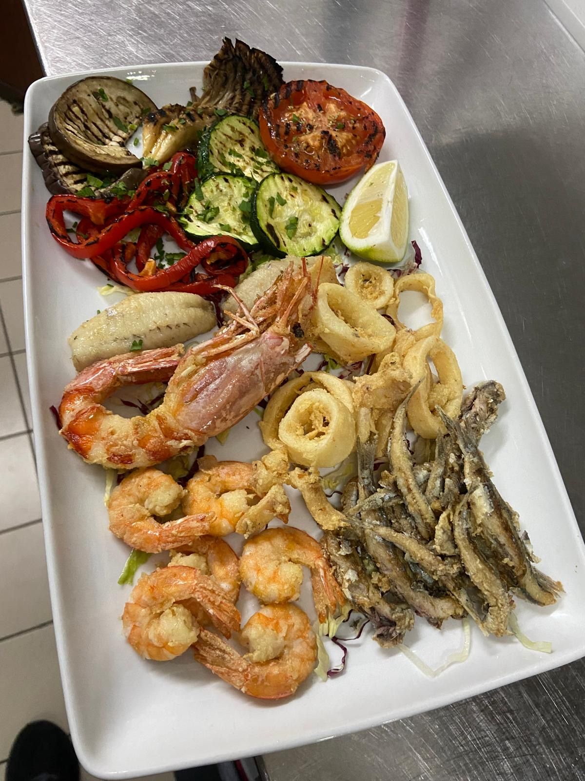 Un piatto bianco con sopra gamberi e verdure su un tavolo.