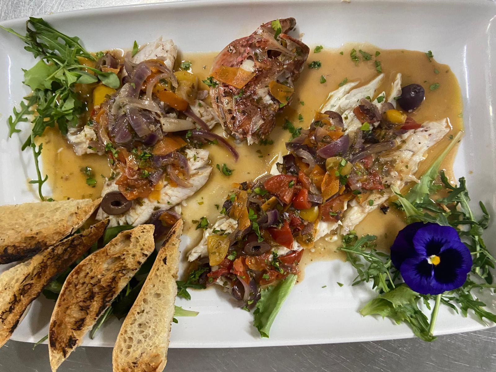 Un piatto bianco sormontato da vari cibi e da un fiore.