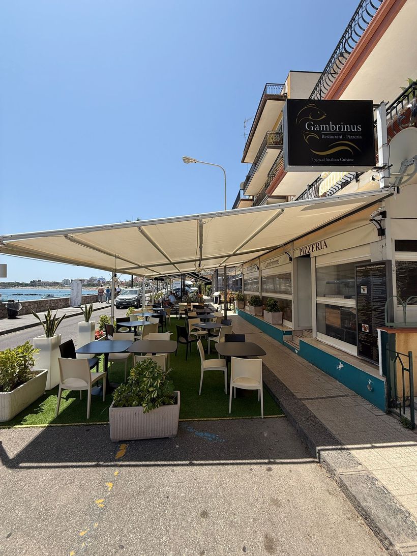 Un ristorante con tavoli e sedie sotto gli ombrelloni in una giornata di sole.