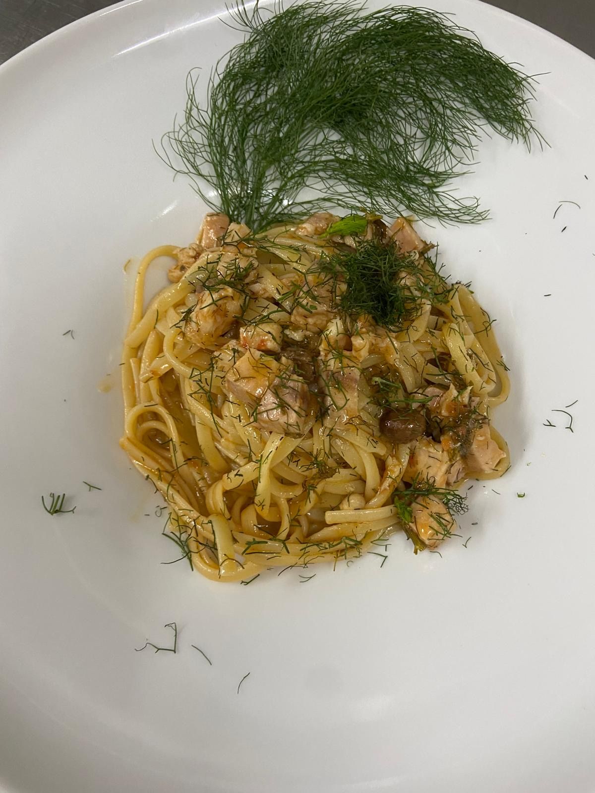 Un piatto bianco con sopra tagliatelle e aneto su un tavolo.