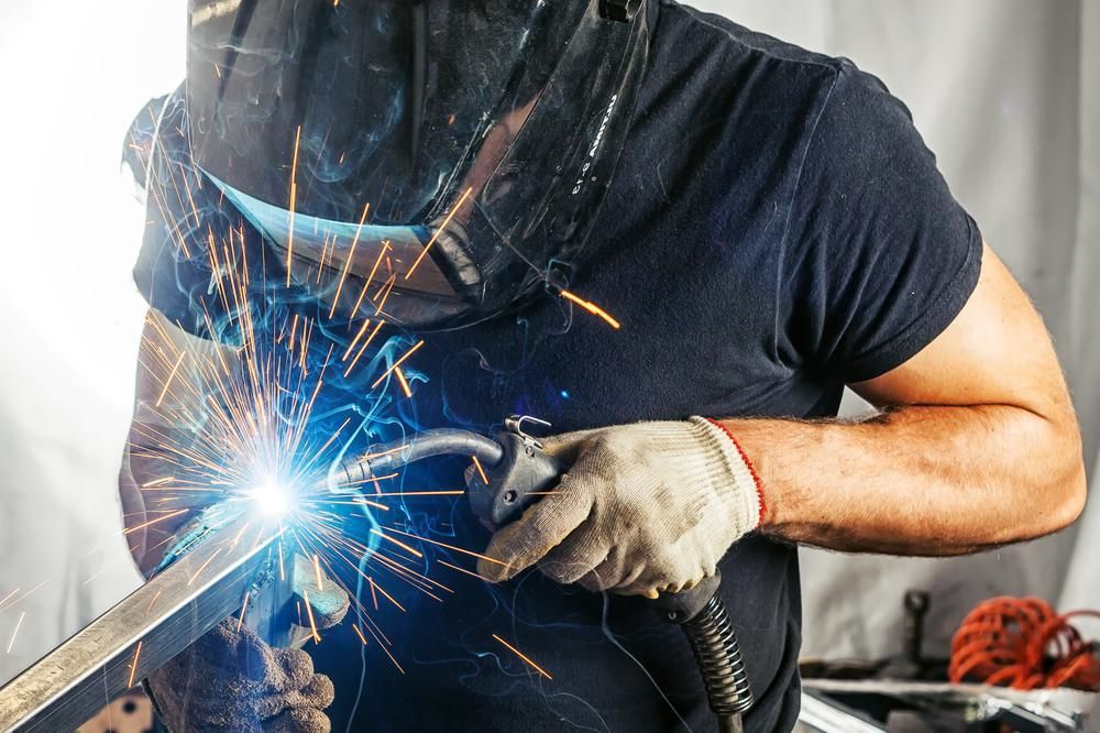 A Man Is Welding a Piece of Metal with A Welding Machine — K & S Sheetmetal in Gladstone Central, QLD