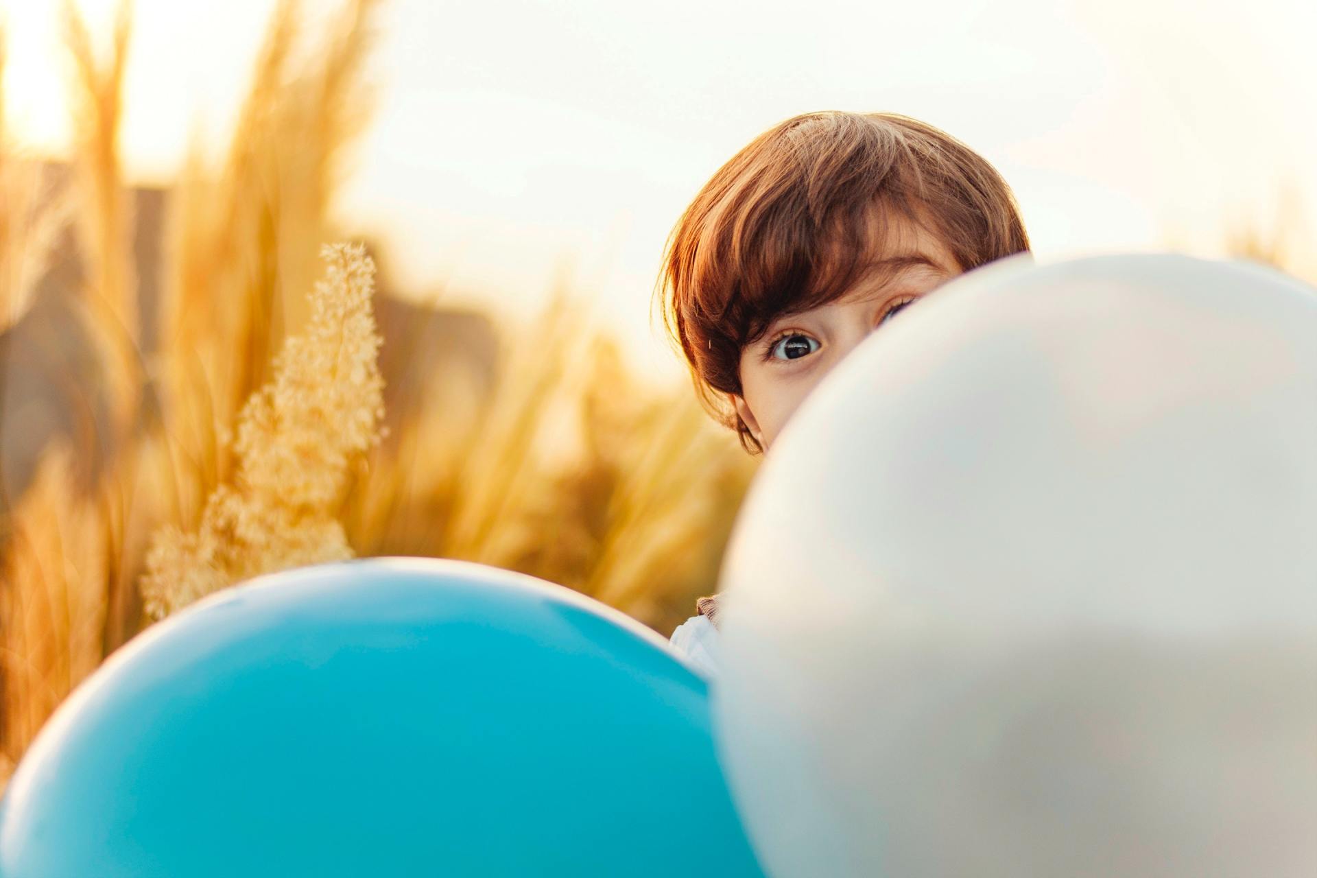 Child peeking out from behind balloons
