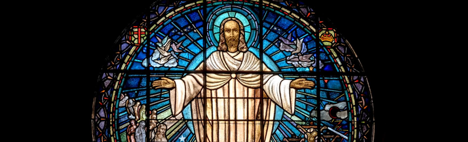 Stained glass window with an image of Jesus holding his hands out to either side.