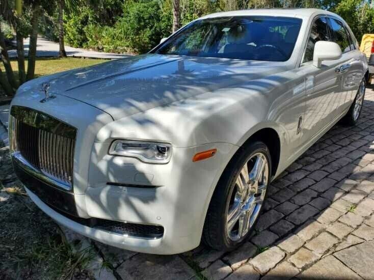 A white rolls royce ghost is parked on a brick driveway.