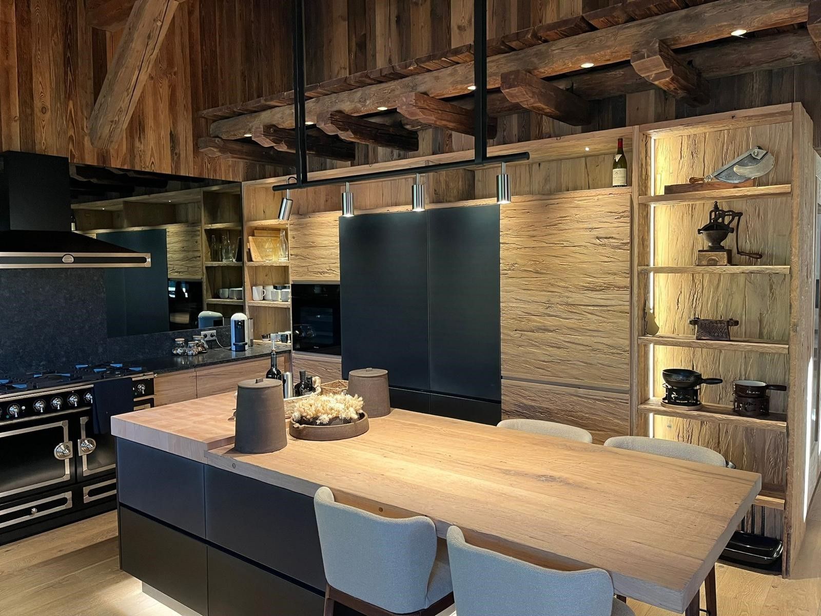 Cuisine moderne avec îlot en bois, armoires et poutres apparentes; électroménagers noirs.