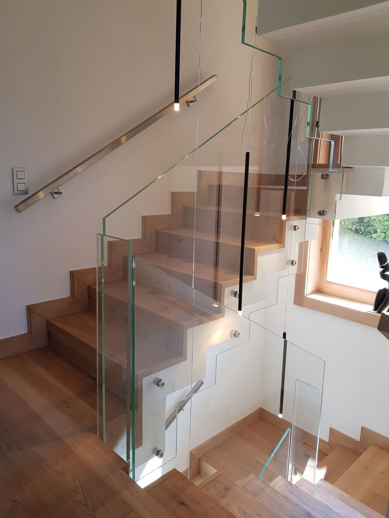 Escalier en bois avec garde-corps en verre. Rambarde en acier inoxydable. Lumière naturelle.