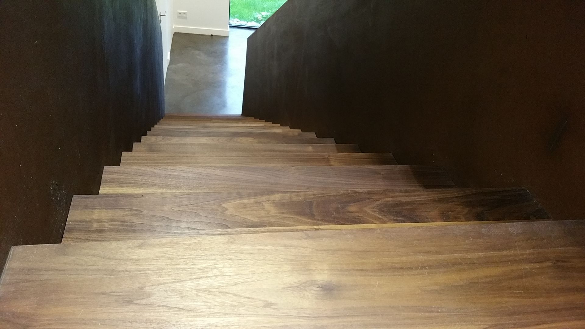 Escalier en bois descendant, murs brun foncé de chaque côté, vue d'en haut.