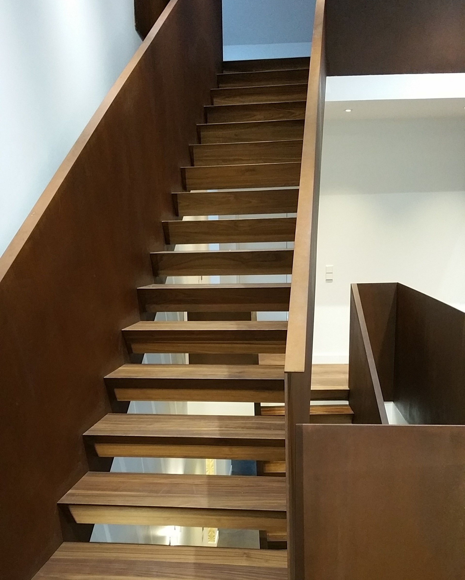 Escalier en bois avec panneaux latéraux brun foncé et marches brun clair, menant vers l'étage dans un cadre moderne.