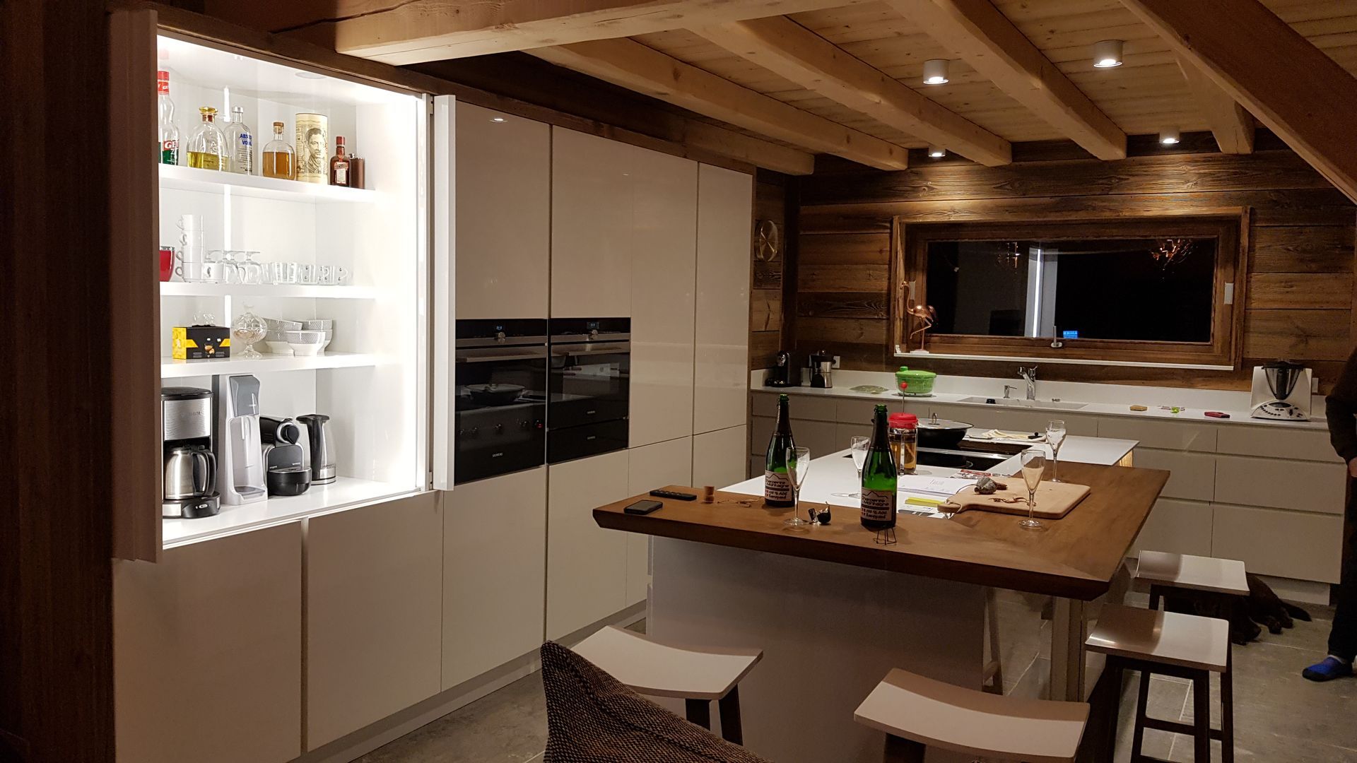 Cuisine moderne avec placards clairs, éléments en bois et îlot central avec tabourets.