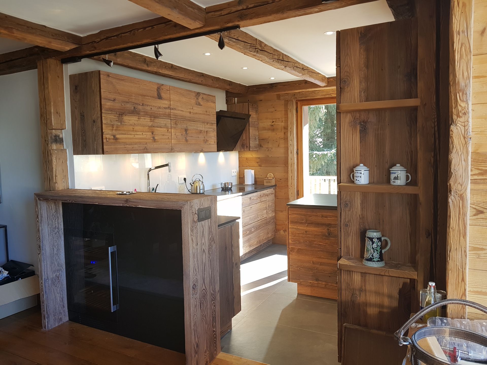 Cuisine rustique en bois avec poutres apparentes, placards et îlot central ; électroménager noir.