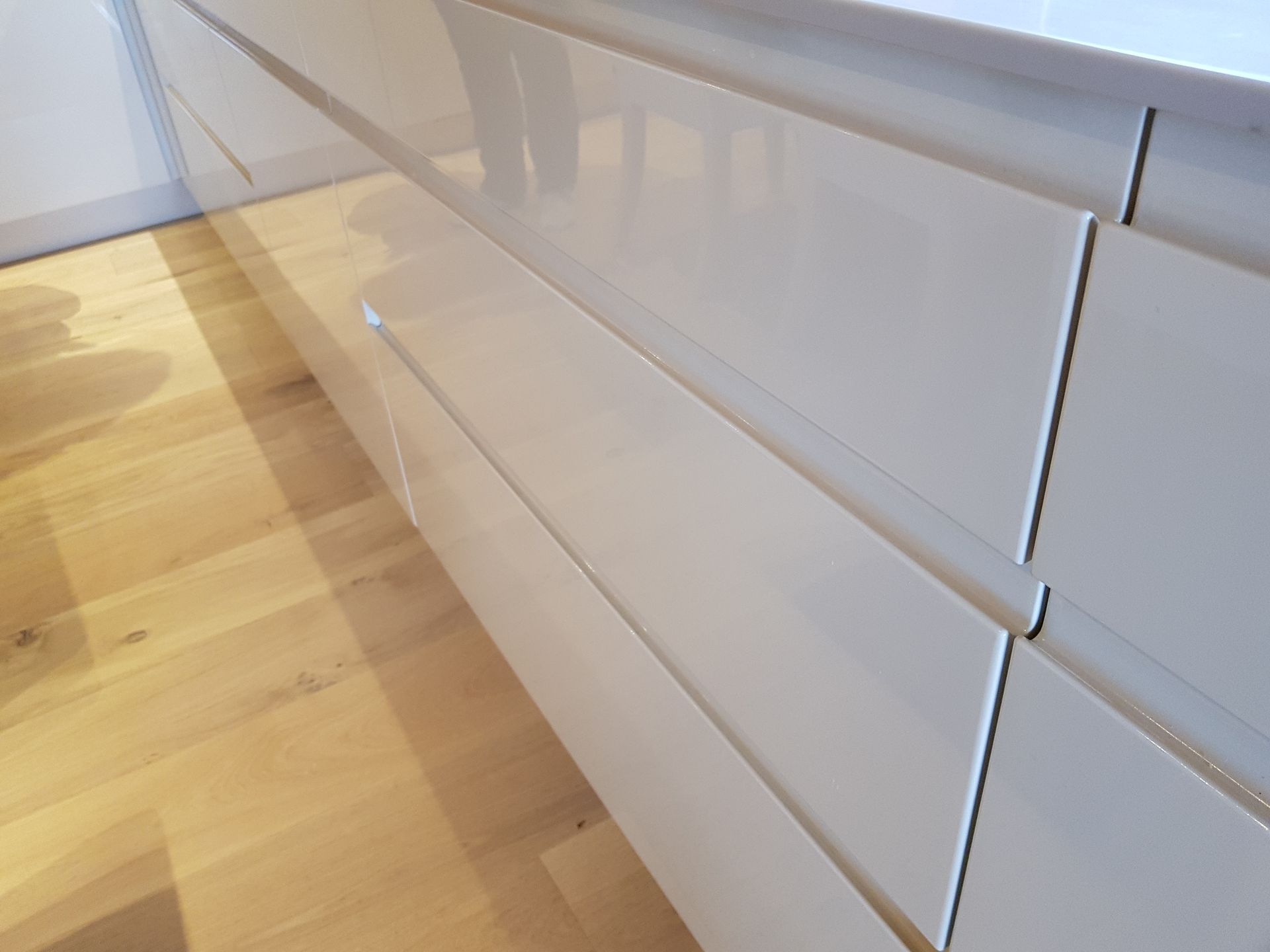 Gros plan sur des tiroirs de placard de cuisine blancs et brillants, avec un sol en bois clair.