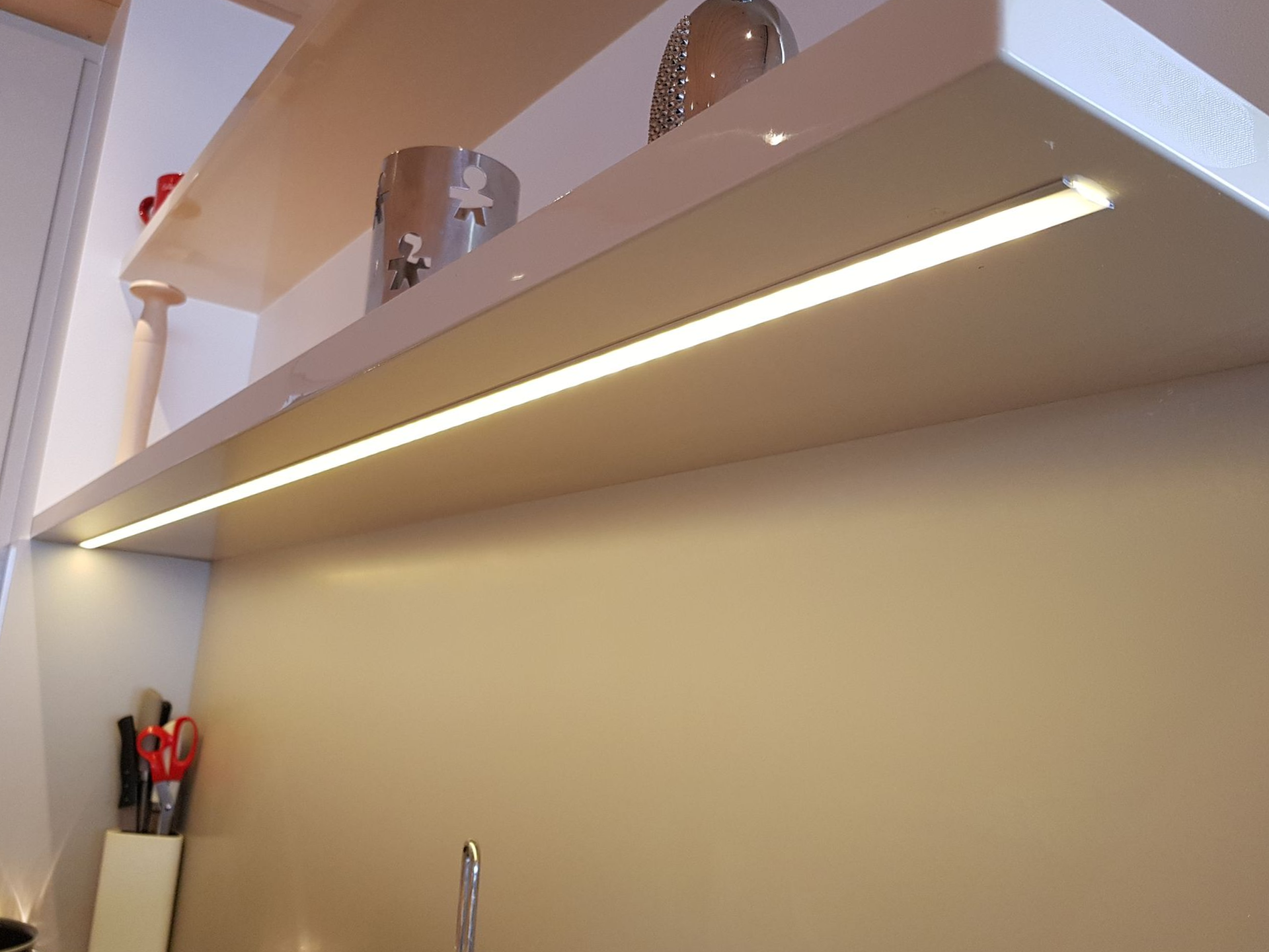 Une étagère avec éclairage LED intégré illuminant un mur aux tons neutres ; des objets sur une étagère au-dessus.