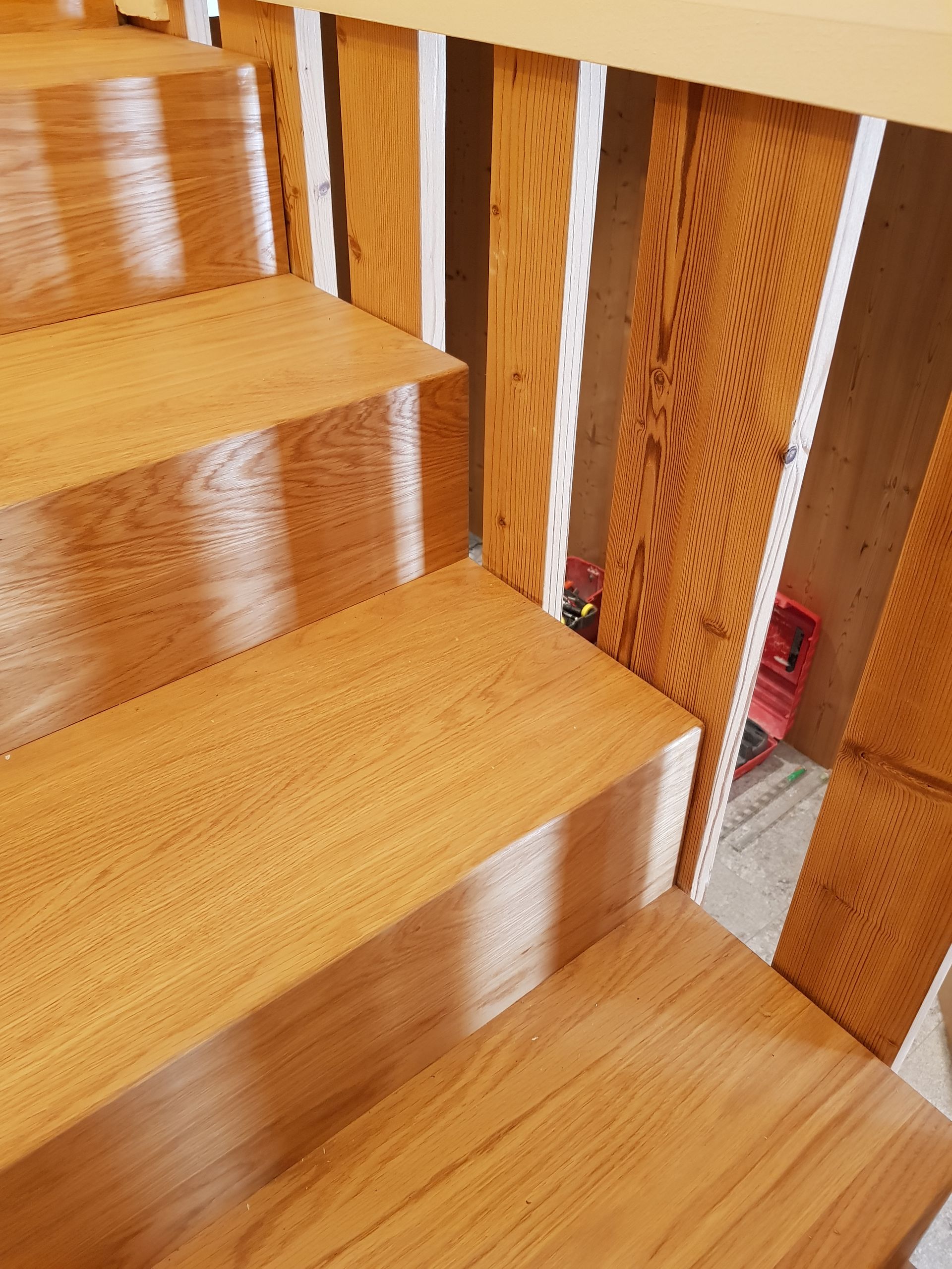 Escalier en bois aux tons chauds. Rambarde et supports verticaux apparents.