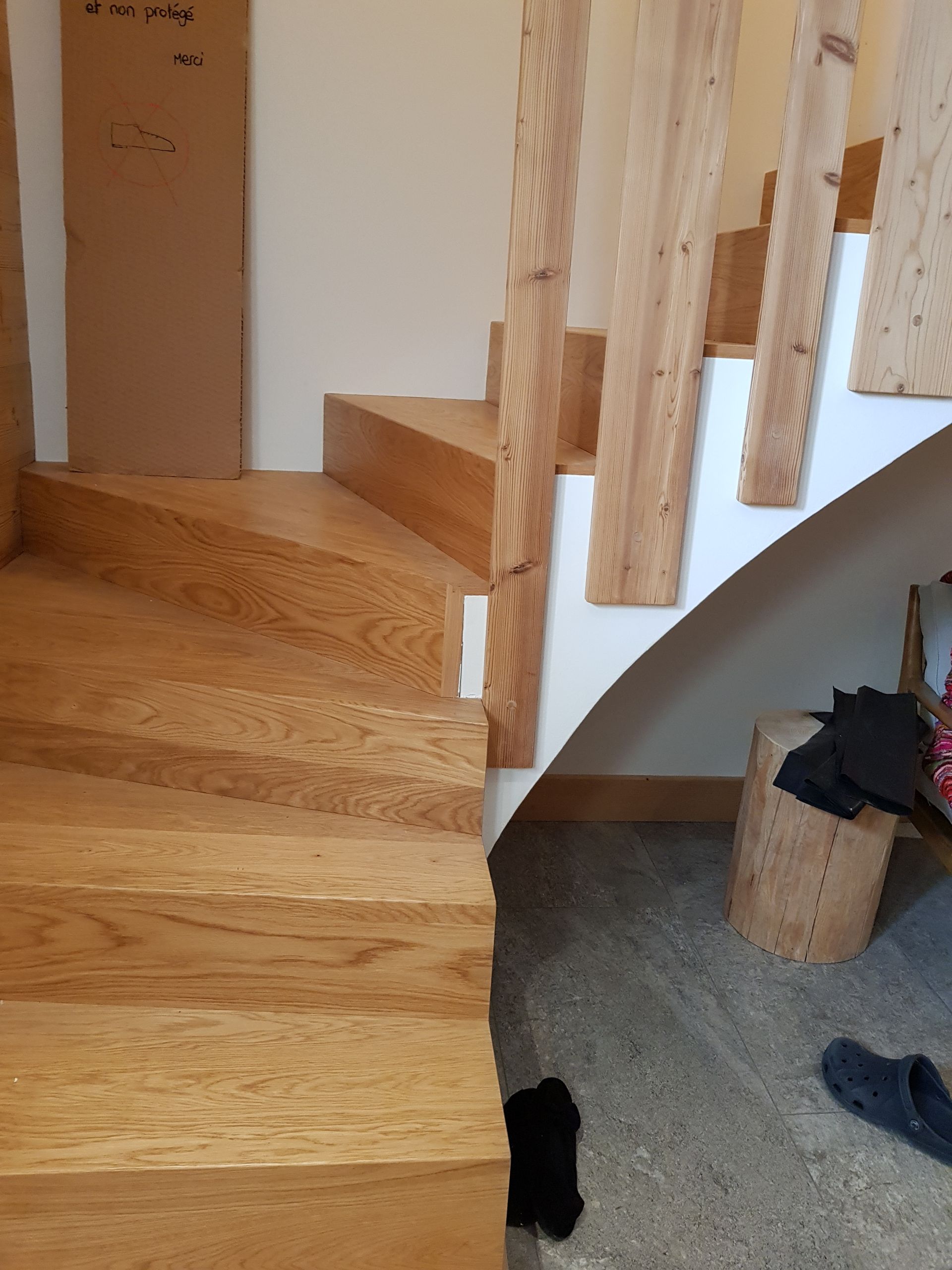 Escalier en bois avec marches et rampe brun clair. Mur blanc et sol gris.